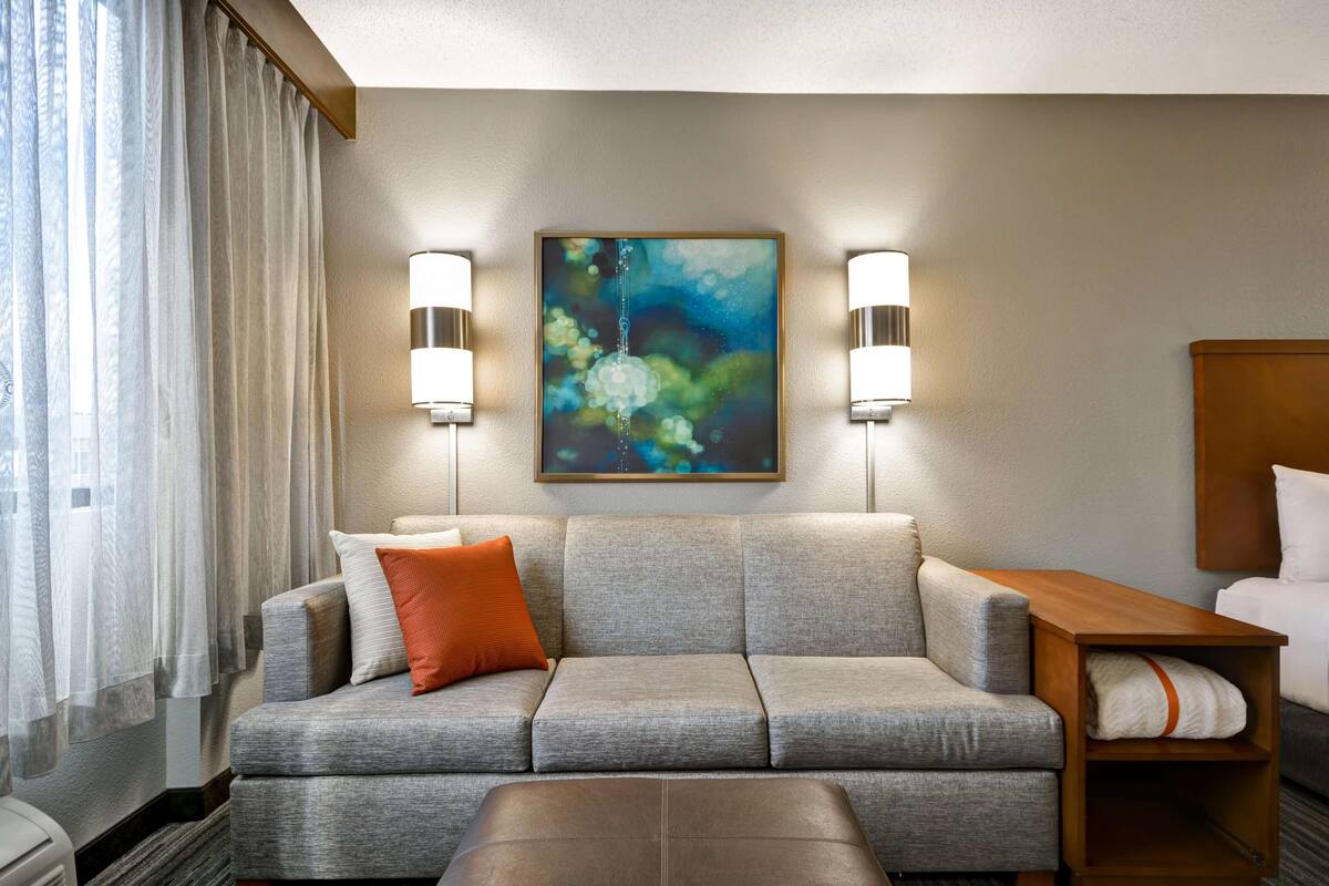 Een moderne hotelkamer met een grijze bank, een houten bijzettafeltje en een schilderij aan de muur.