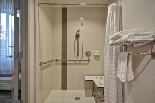 Un baño con ducha, barras de apoyo, toallero y retrete.