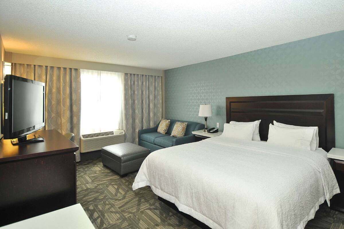 A hotel room with a large bed, a television, a sofa, a desk, and a lamp.