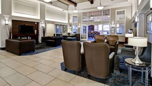 A spacious lobby with a large seating area, a television mounted on a wooden panel, and a view of the outside through large windows. - Hampton Inn & Suites by Hilton Calgary-Airport (Calgary)