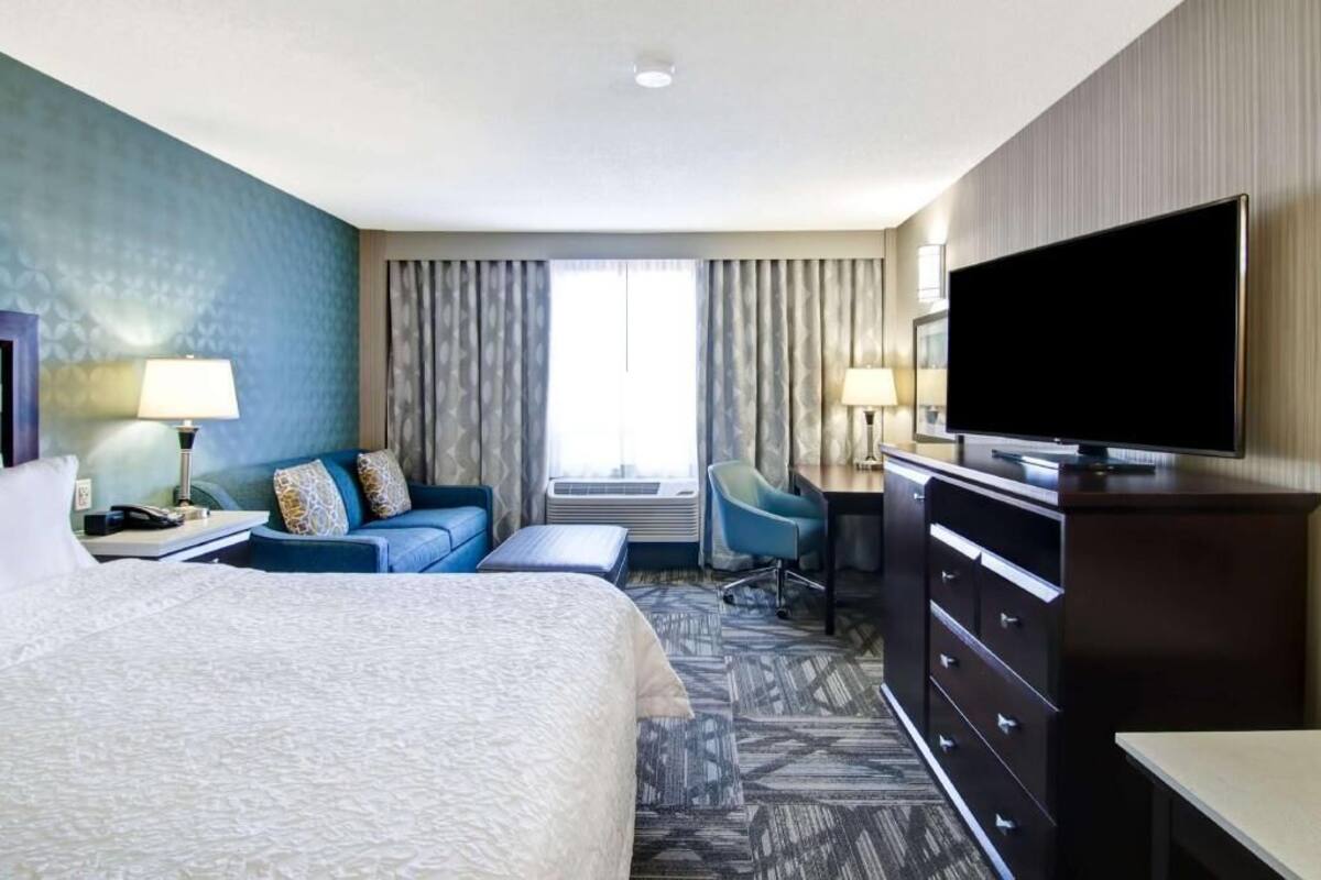 A hotel room with a bed, a desk, a chair, a TV, and a window with curtains.