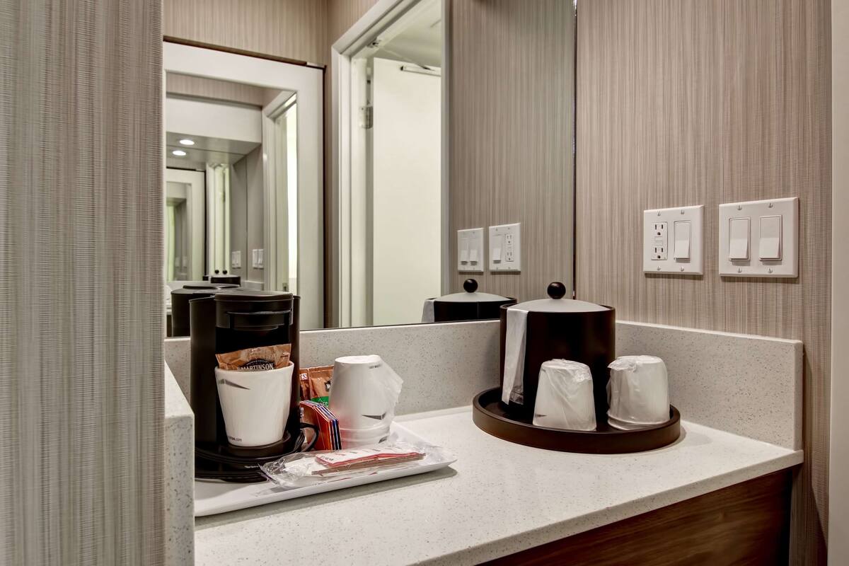 A hotel bathroom with a coffee station, a mirror, and a sink.