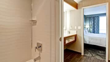 A hotel room with a shower, a wooden vanity, a bed, and a view of the outside.