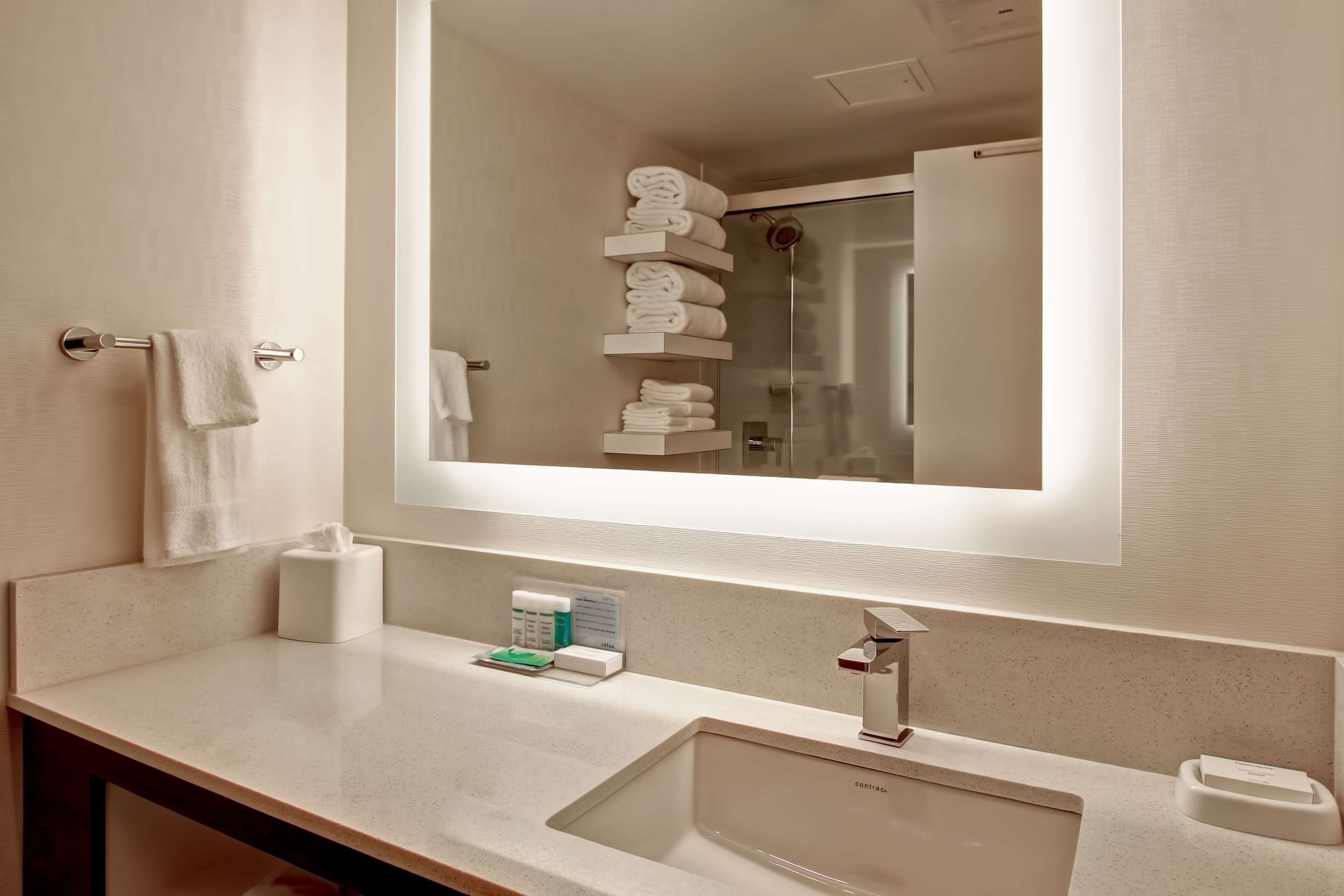 A bathroom with a large mirror, a sink, and a towel rack.