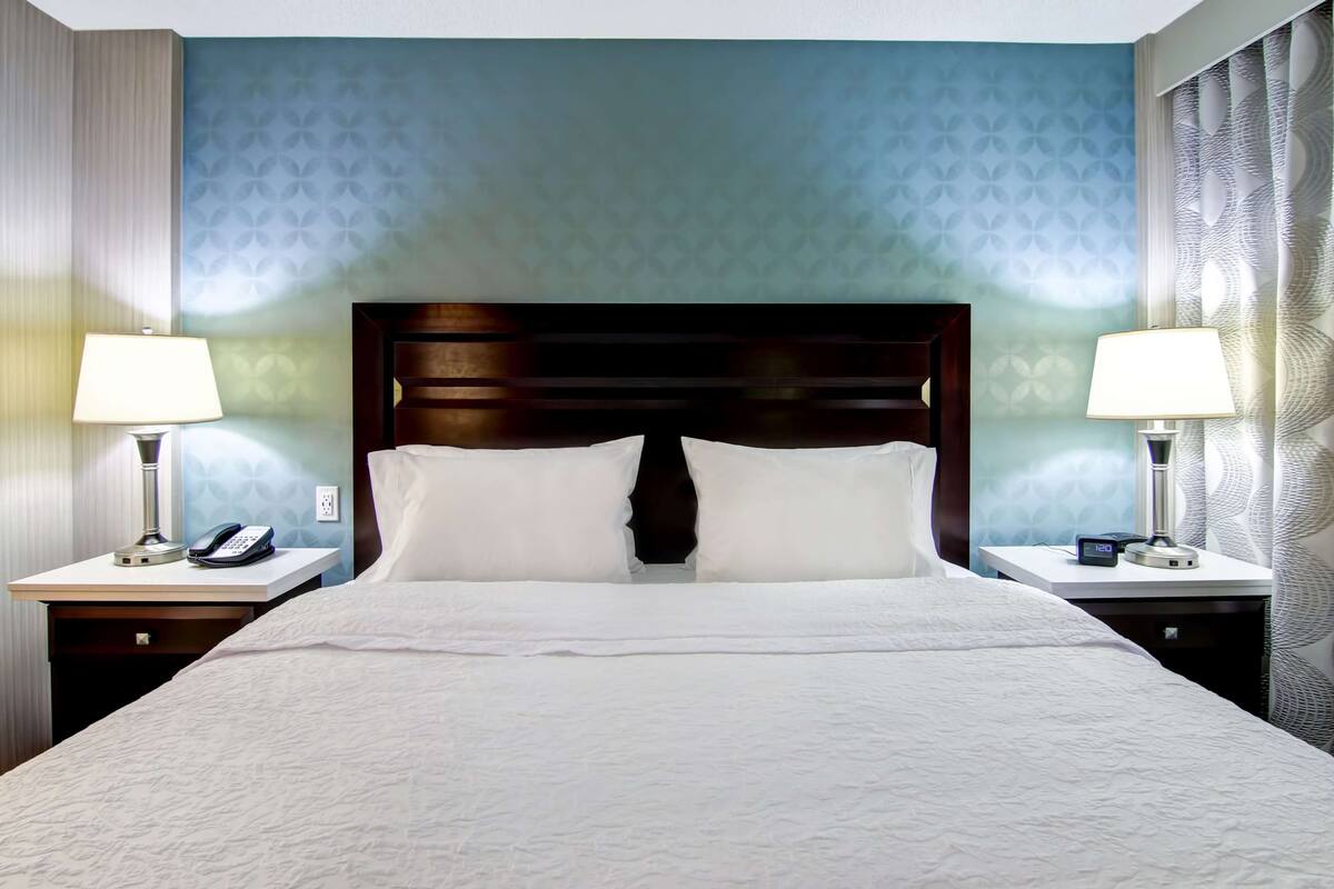 A hotel room with a large bed, two bedside tables with lamps, a phone, and a clock.