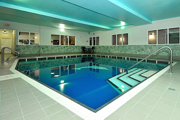 An indoor swimming pool with clear lanes, a changing room, and a staircase leading to the pool.