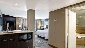 A modern hotel room with a kitchenette, a bed with a white duvet, a bathroom with a bathtub, and a large mirror. - Hampton Inn & Suites by Hilton Calgary-Airport (Calgary)