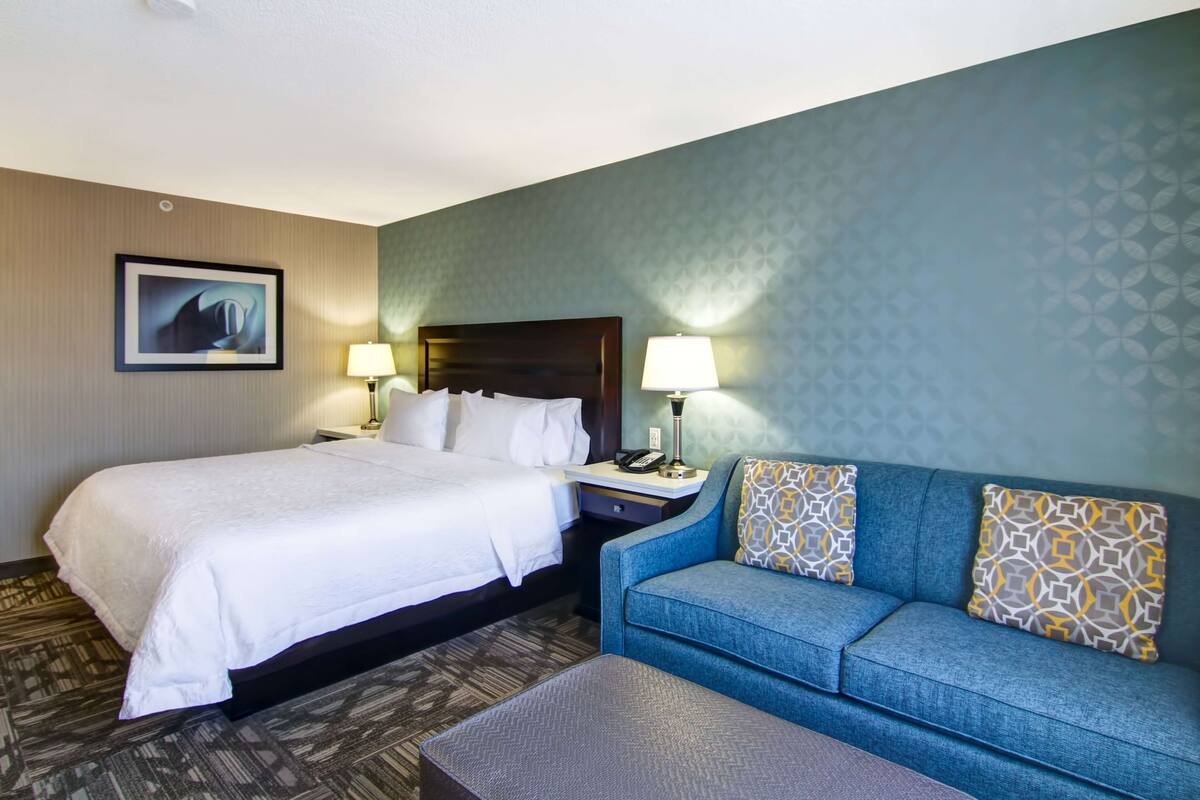 A hotel room with a large bed, a sofa, two bedside tables with lamps, and a framed picture on the wall.