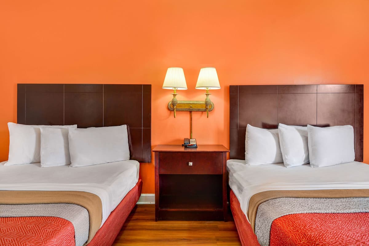 A hotel room with two beds, a nightstand with lamps, and a wooden headboard.