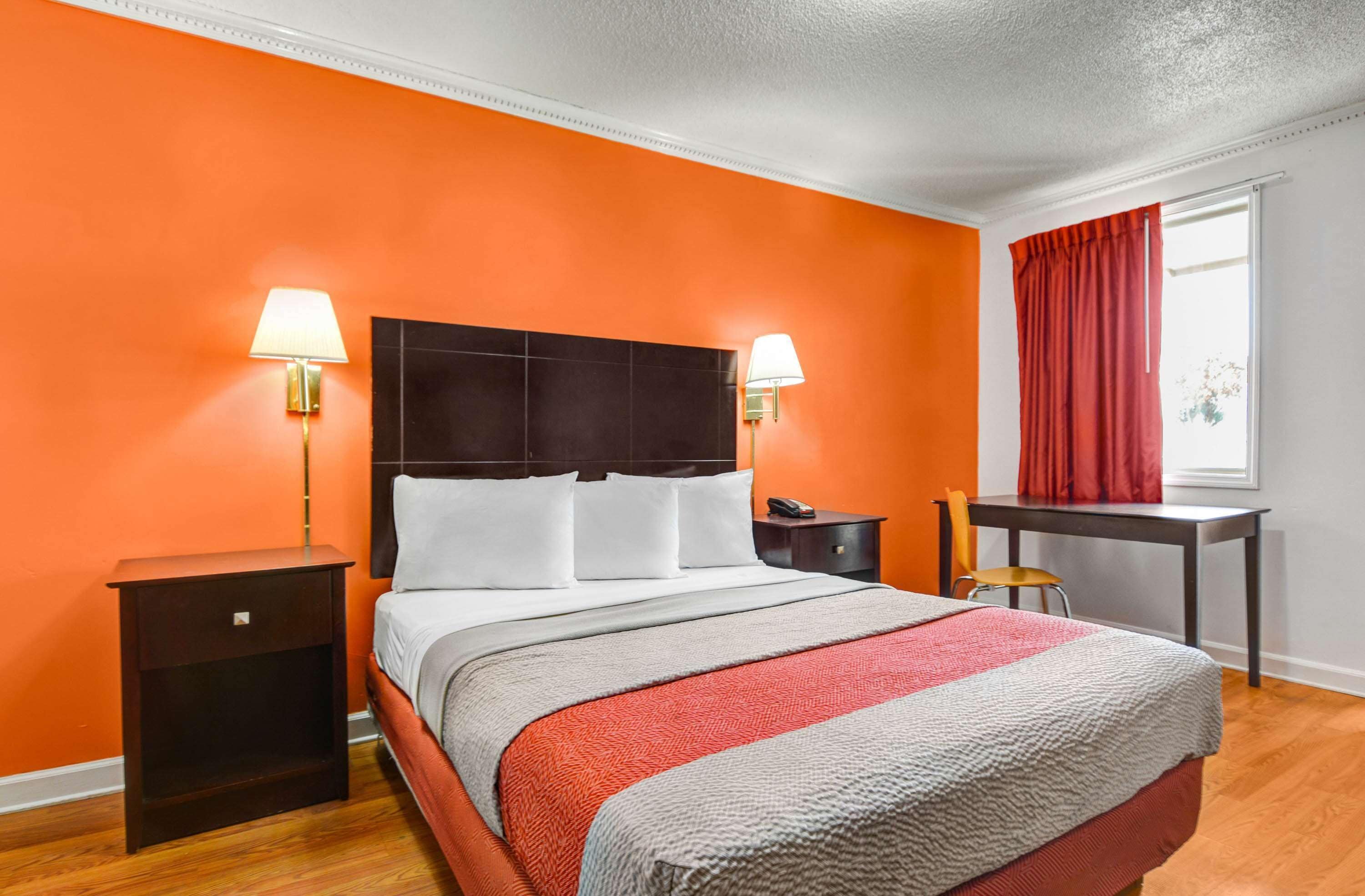Une chambre d’hôtel avec un grand lit, deux tables de chevet, un bureau et une fenêtre avec des rideaux rouges.