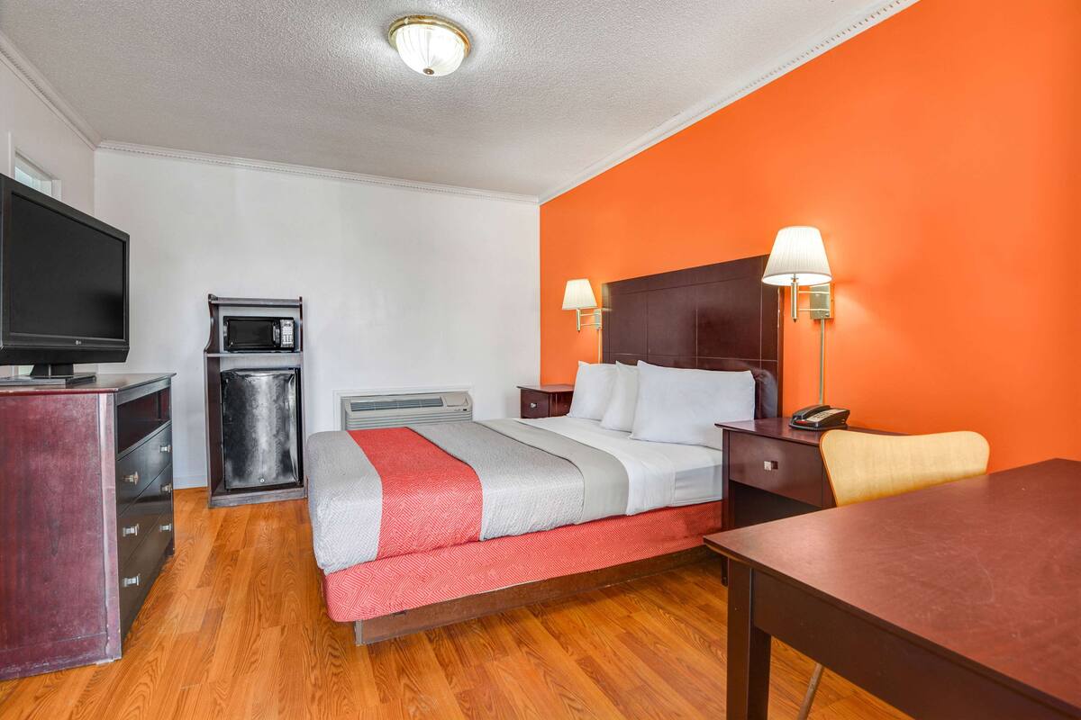 A hotel room with a bed, a desk, a television, a microwave, and two wall-mounted lamps.