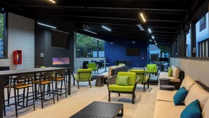 A modern outdoor seating area with bar stools, green chairs, and a sofa. - Hampton Inn & Suites Alpharetta Roswell (Alpharetta)