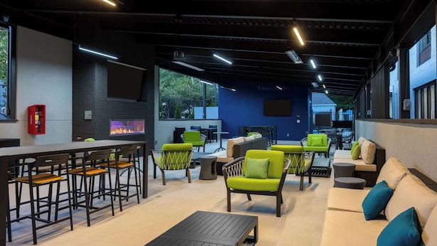 A modern outdoor seating area with bar stools, green chairs, and a sofa. - Hampton Inn & Suites Alpharetta Roswell (Alpharetta)