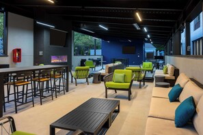 A modern outdoor seating area with bar stools, green chairs, and a sofa. - Hampton Inn & Suites Alpharetta Roswell (Alpharetta)