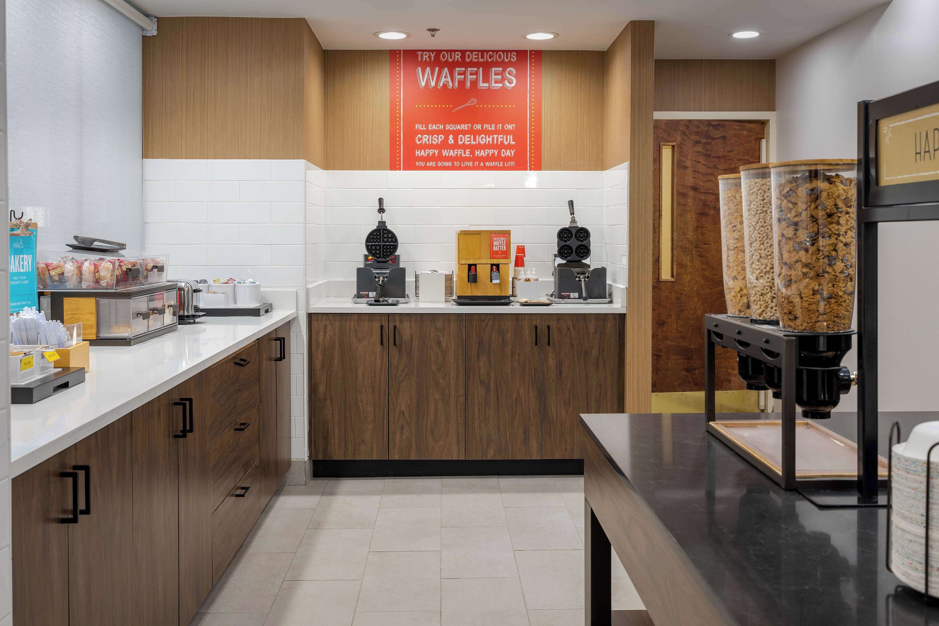 A modern kitchen area with waffle-making equipment, a coffee machine, and a waffle dispenser.