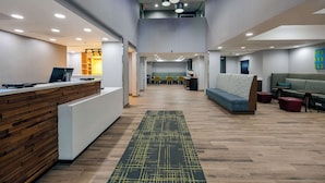A modern reception area with a wooden reception desk, a patterned rug, and seating areas with sofas and chairs. - Hampton Inn & Suites Alpharetta Roswell (Alpharetta)
