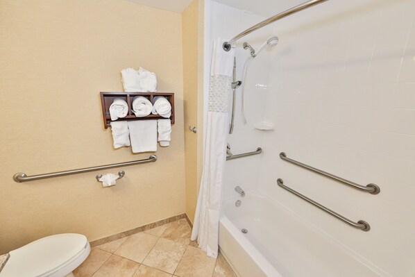 A bathroom with a toilet, a towel rack with towels, a shower with grab bars, and a bathtub.
