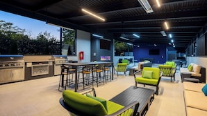 An outdoor patio area with a grill, seating, and a TV screen. - Hampton Inn & Suites Alpharetta Roswell (Alpharetta)