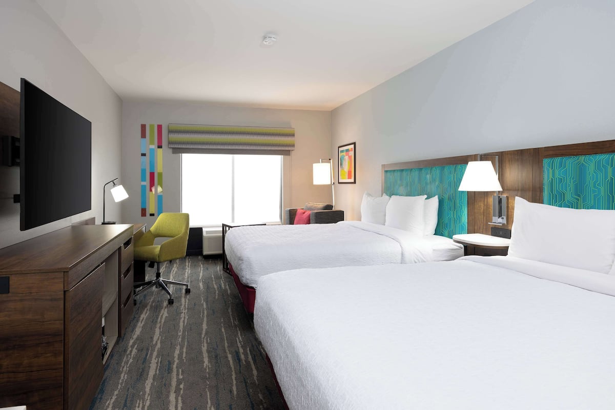 A hotel room with two beds, a desk, a chair, a TV, and a window with a view.