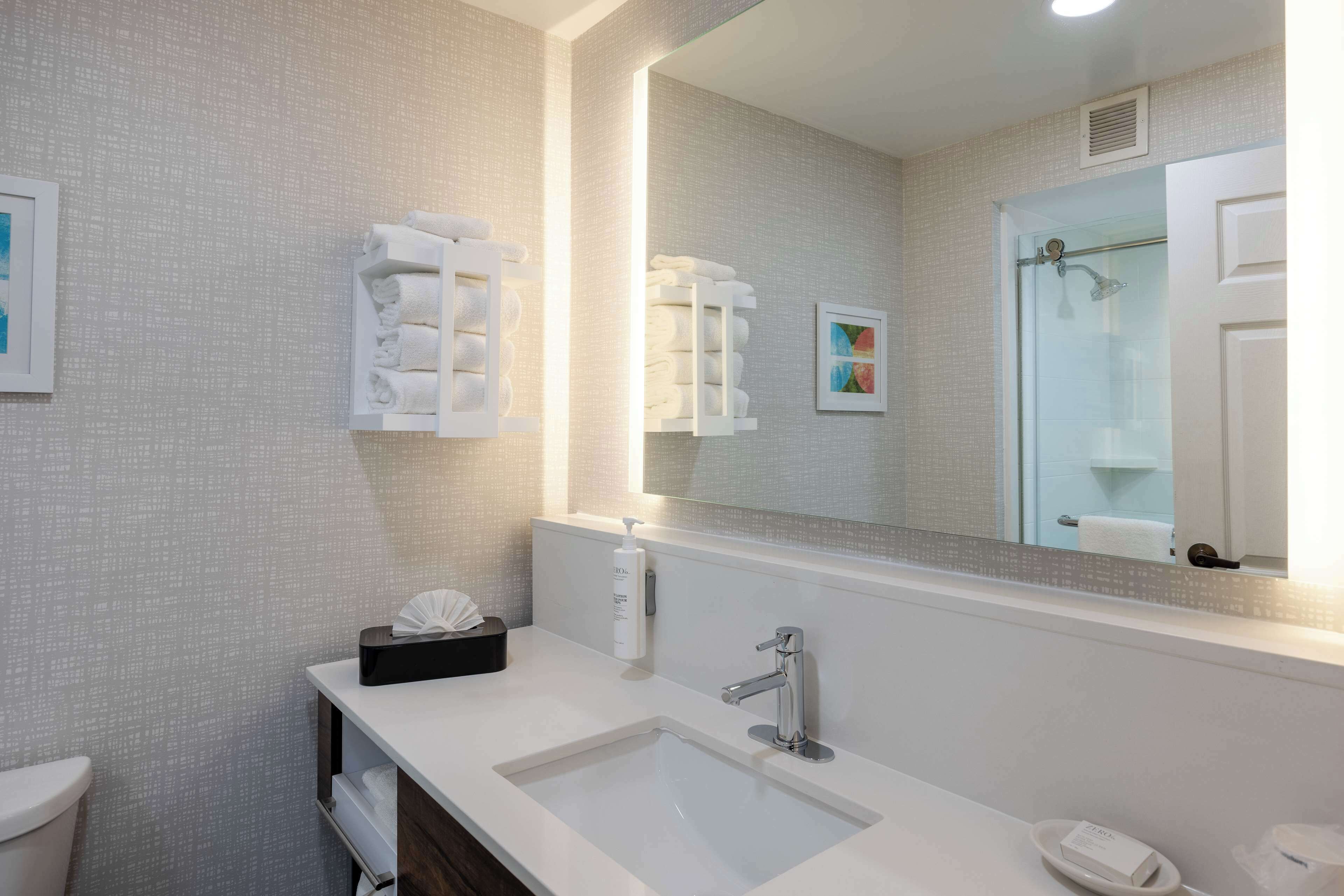 A modern bathroom with a large mirror, a white sink, and neatly stacked towels.
