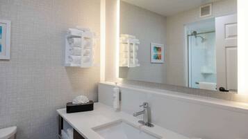 A modern bathroom with a large mirror, a white sink, and neatly stacked towels.