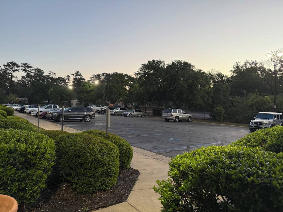 A parking lot with multiple cars, surrounded by well-maintained hedges and trees.