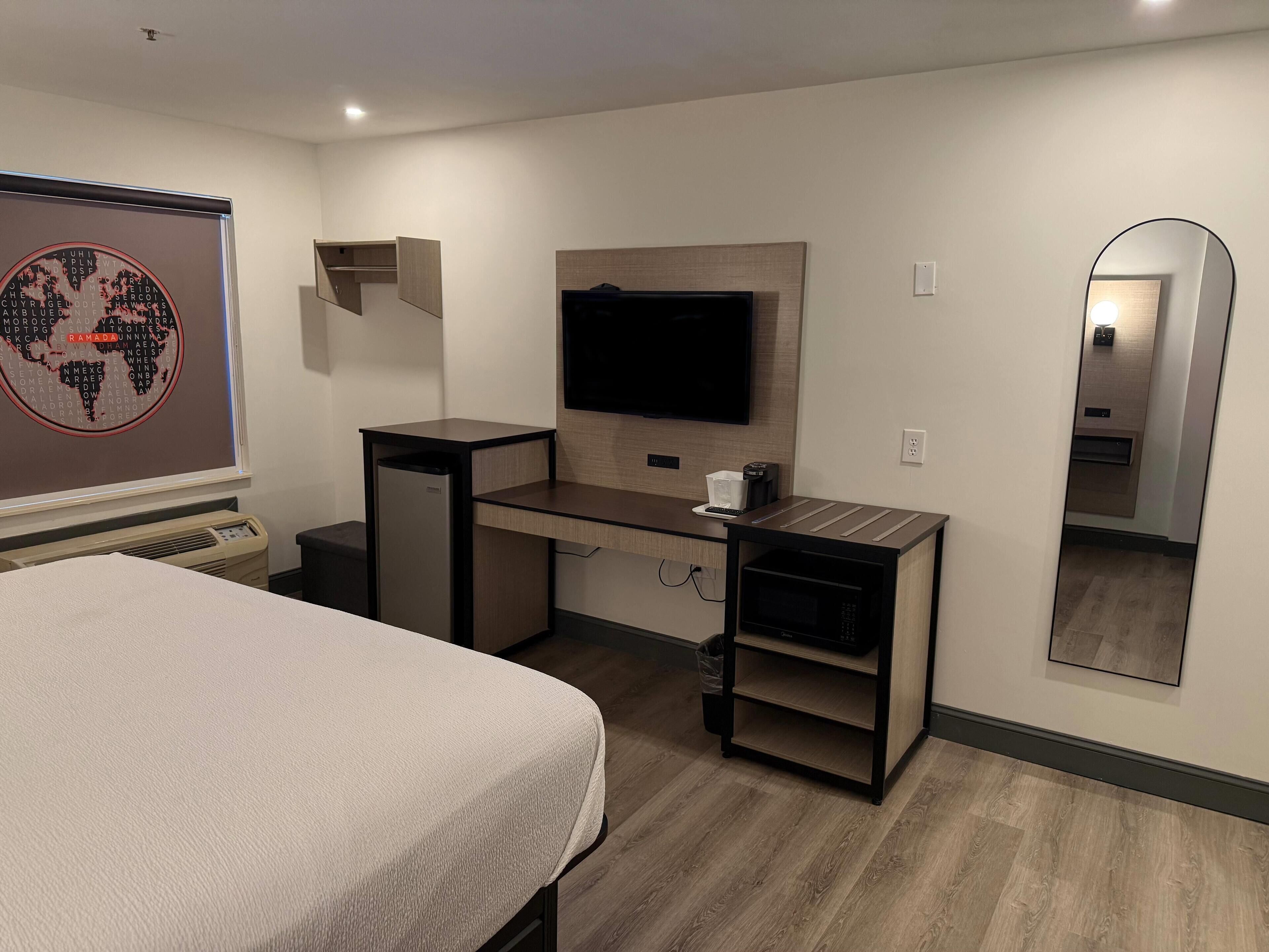 A modern hotel room with a bed, a desk with a flat-screen TV, a wall-mounted mirror, and a world map artwork.