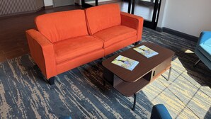 A lobby with an orange sofa, a wooden coffee table with magazines, and a reception desk. - Ramada by Wyndham Albany GA (Albany)
