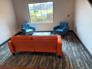 A room with a large window, two blue armchairs, an orange sofa, and a small table with books. - Ramada by Wyndham Albany GA (Albany)