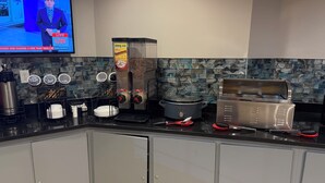 A kitchen with a coffee maker, a slow cooker, a toaster, and a TV displaying a news broadcast. - Ramada by Wyndham Albany GA (Albany)