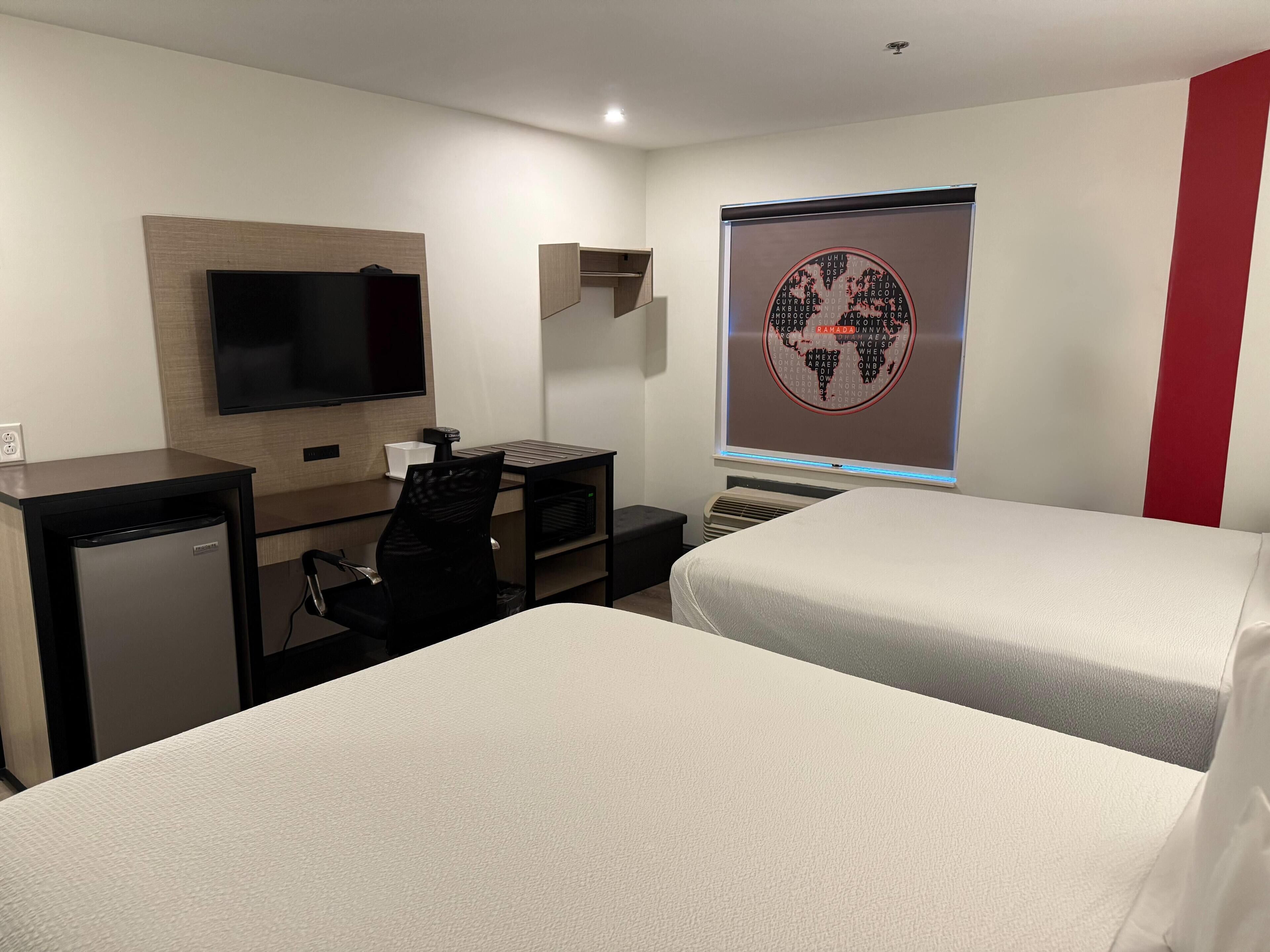 Une chambre d’hôtel avec deux lits, un bureau avec un ordinateur, une télévision et une carte du monde accrochée au mur.
