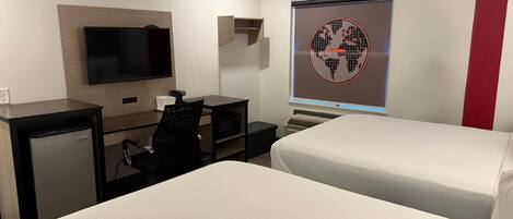A hotel room with two beds, a desk with a computer, a TV, and a world map on the wall.