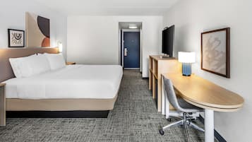 A hotel room with a bed, desk, chair, TV, and artwork.
