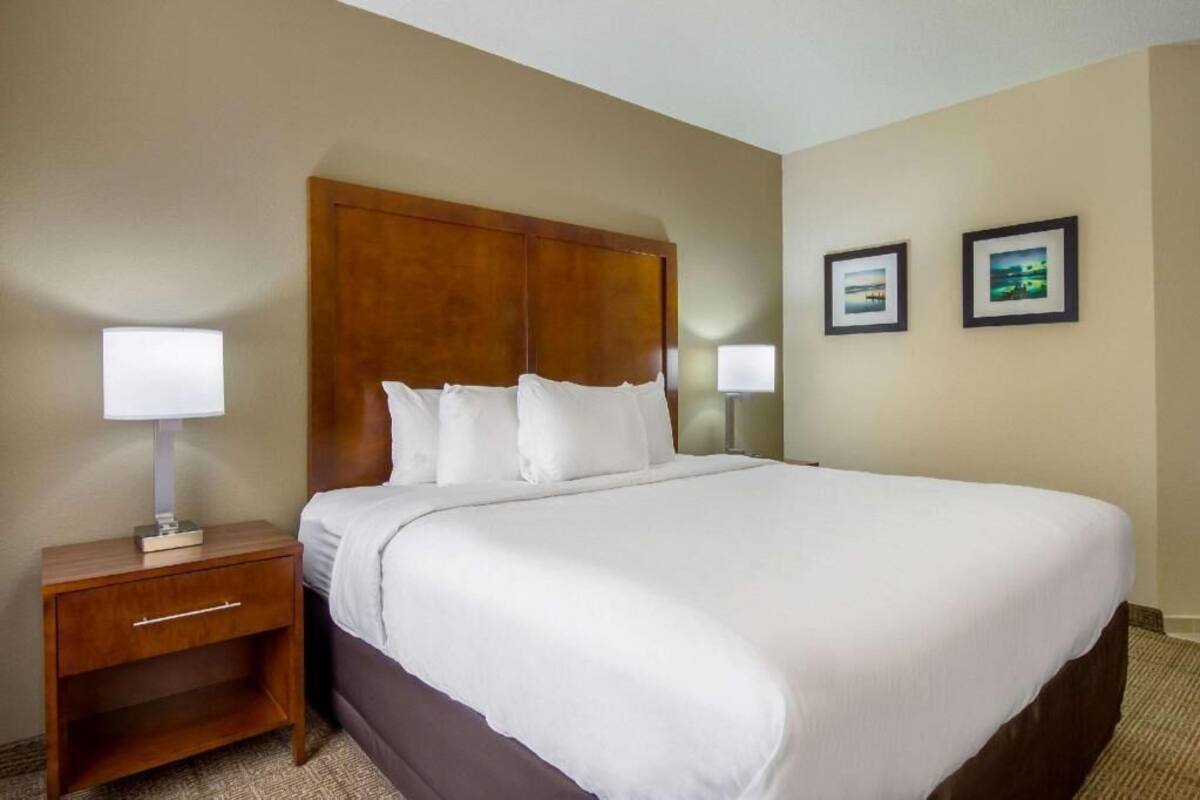 A hotel room with a large bed, a wooden headboard, a nightstand with a lamp, and two framed pictures on the wall.