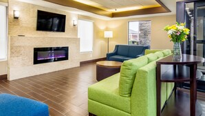 Een moderne woonkamer met een open haard, een groene bank, een blauwe fauteuil en een ronde salontafel.
