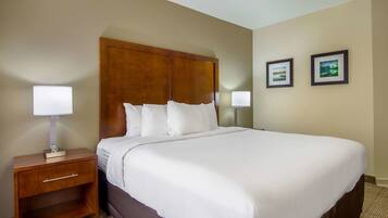 A hotel room with a large bed, a wooden headboard, a nightstand with a lamp, and two framed pictures on the wall.