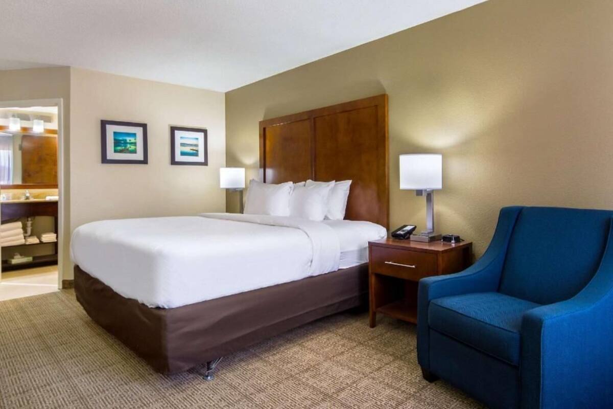 A hotel room with a bed, bedside tables, a chair, and framed pictures on the wall.