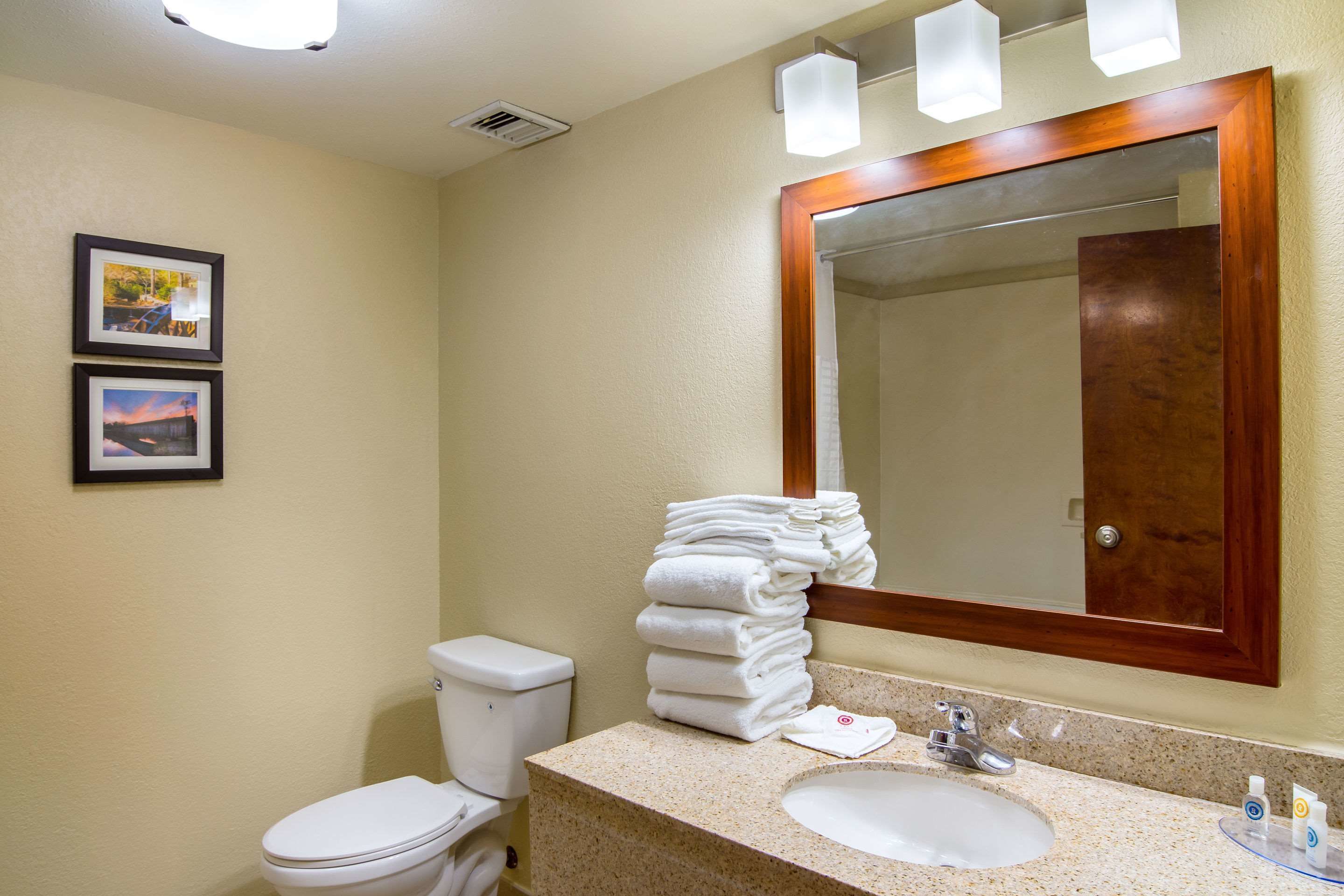 A bathroom with a toilet, sink, and a stack of white towels. There are two framed pictures on the wall.