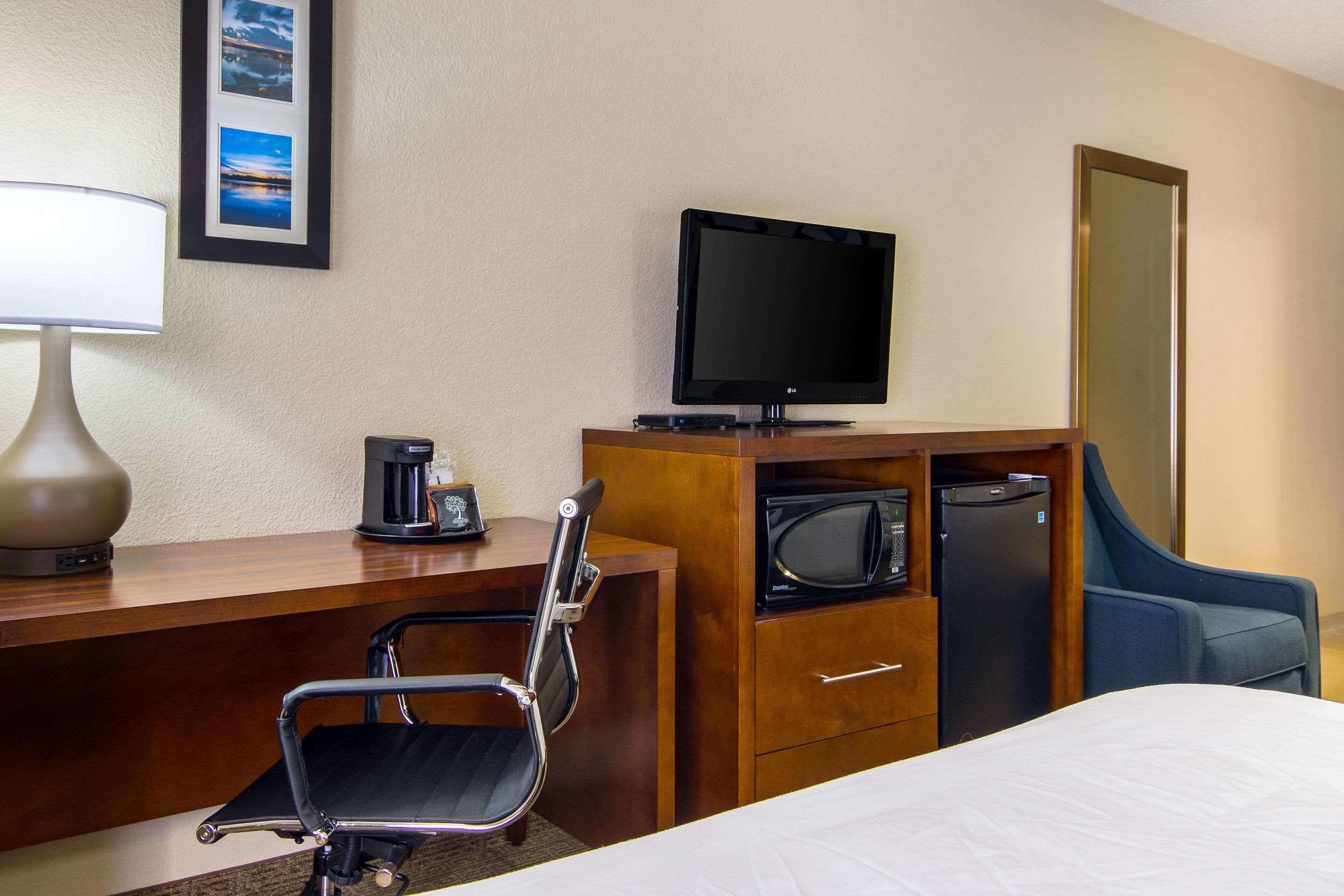 Una habitación de hotel con una cama, un escritorio con lámpara, televisión, microondas, refrigerador y una silla.