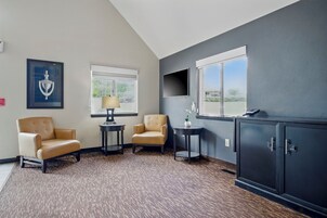 A hotel room with a large window, two armchairs, a small table with a lamp, a cabinet, and a framed picture on the wall.