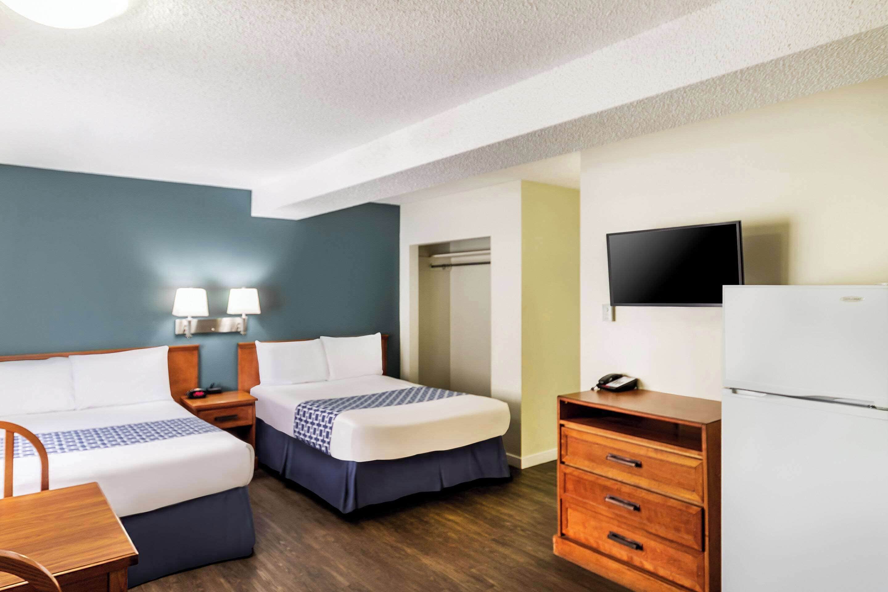 A hotel room with two beds, a desk, a chair, a dresser, a TV, and a refrigerator.