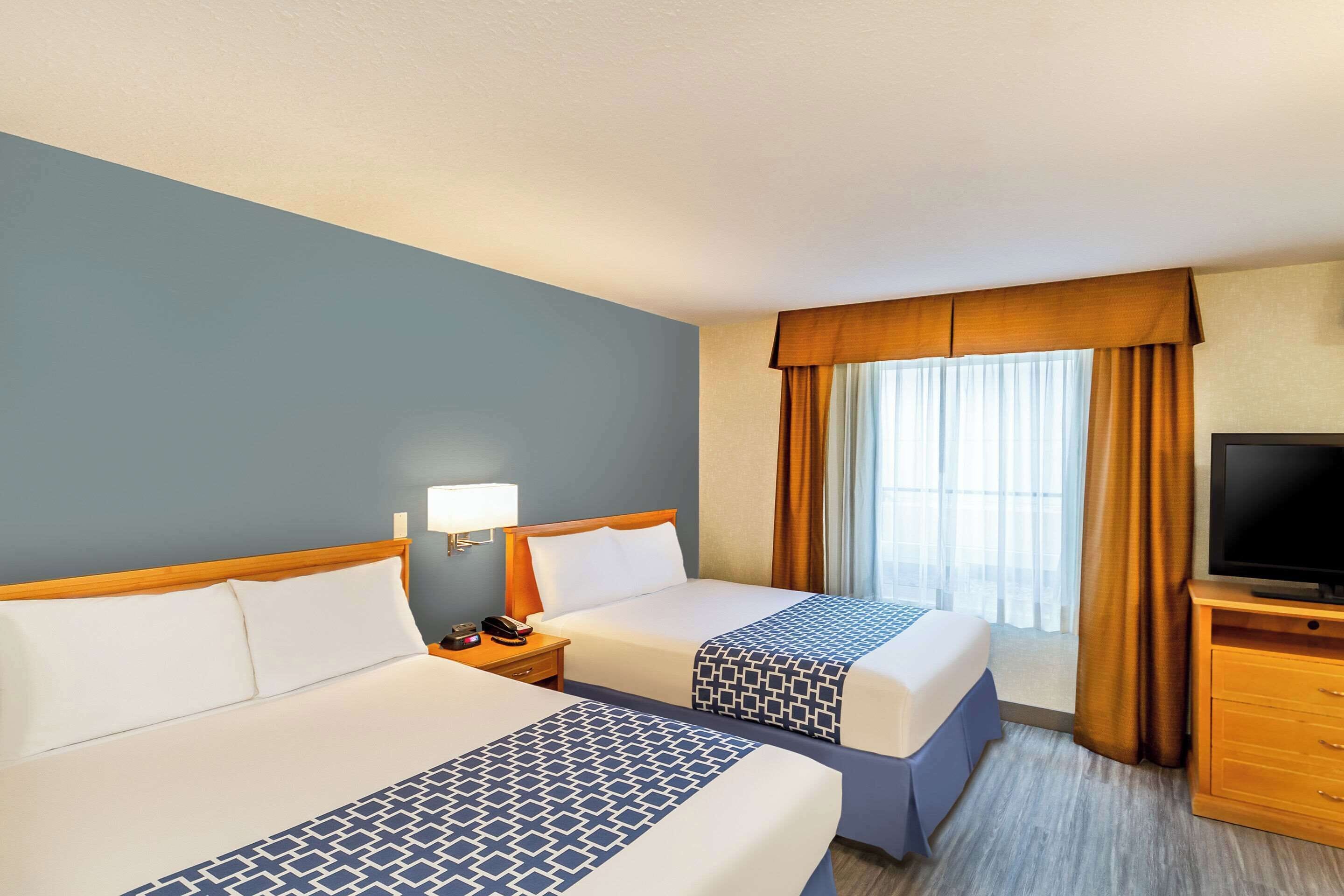 Una habitación de hotel con dos camas, televisor, mesita de noche y ventana con cortinas.