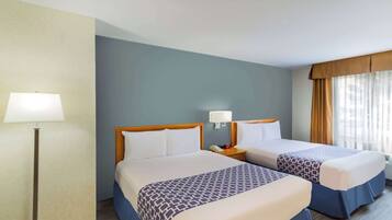 A hotel room with two beds, a nightstand with a lamp, and a window with curtains.