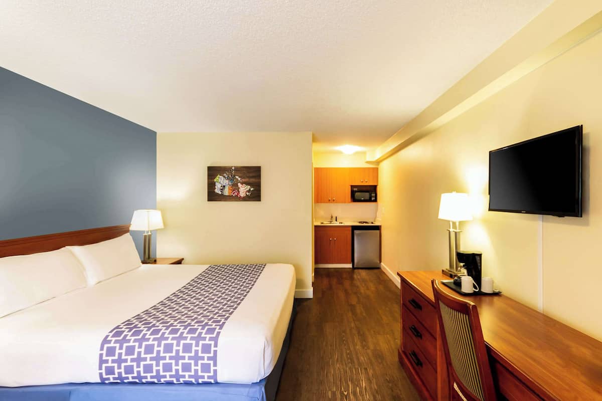 Une chambre d’hôtel équipée d’un lit, d’un bureau, d’une télévision, d’un coin cuisine et d’un téléviseur fixé au mur.
