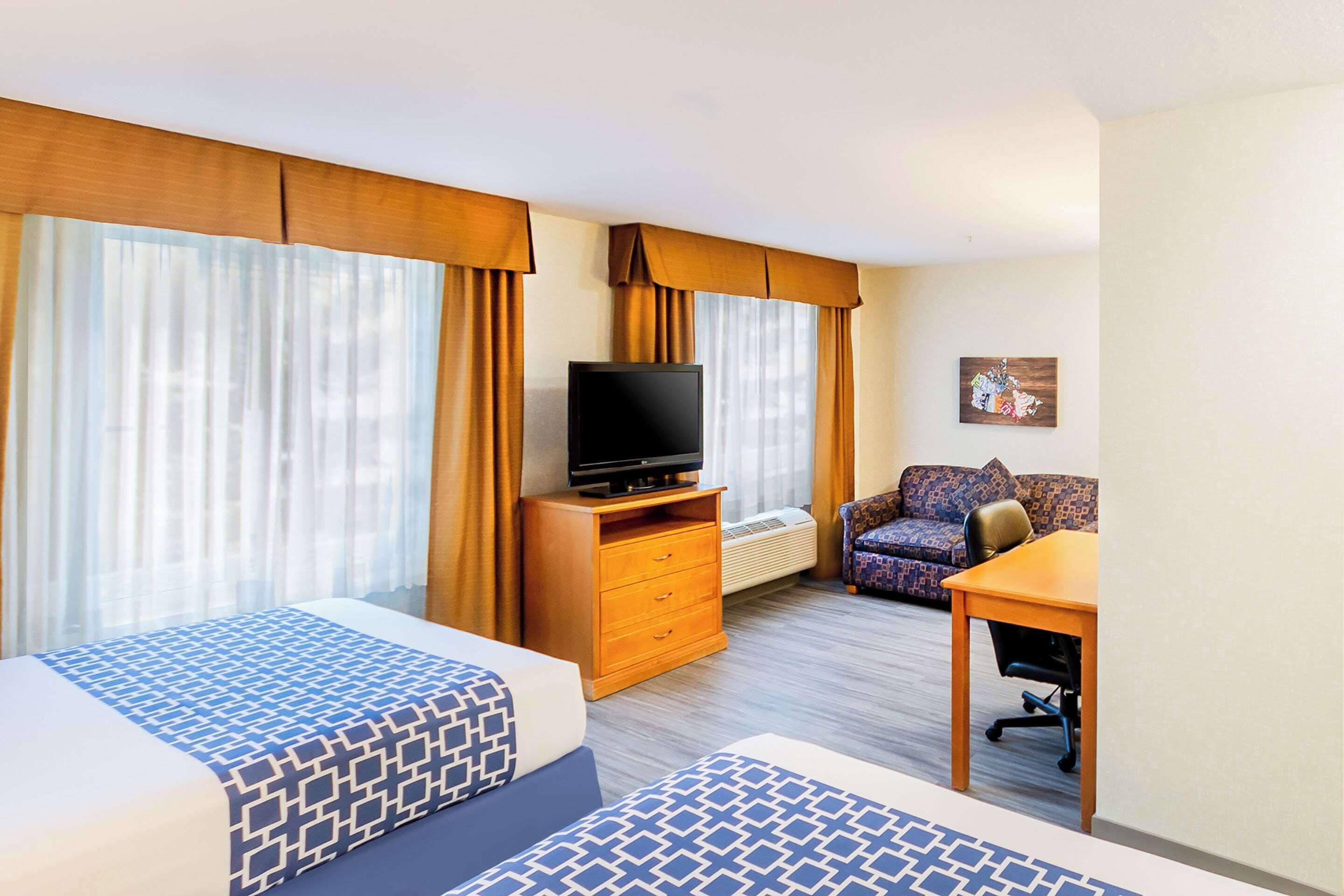A hotel room with two beds, a TV, a sofa, and a small table.