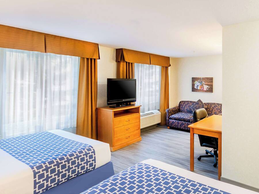 A hotel room with two beds, a TV, a sofa, and a small table.