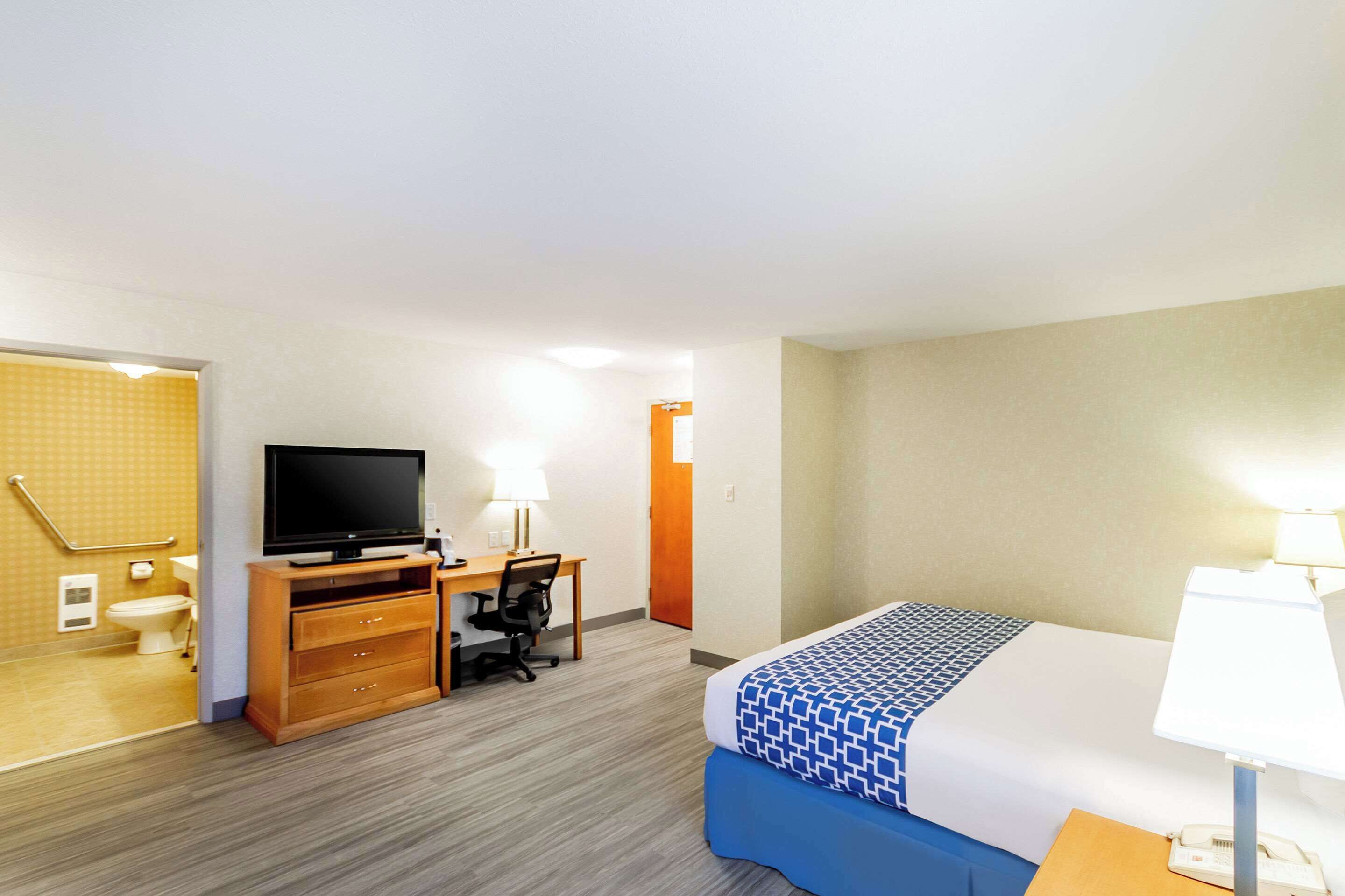 A hotel room with a bed, desk, chair, television, and a bathroom with a toilet and shower.