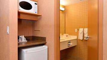 Un baño de hotel pequeño y funcional, con microondas, refrigerador, lavamanos y espejo.