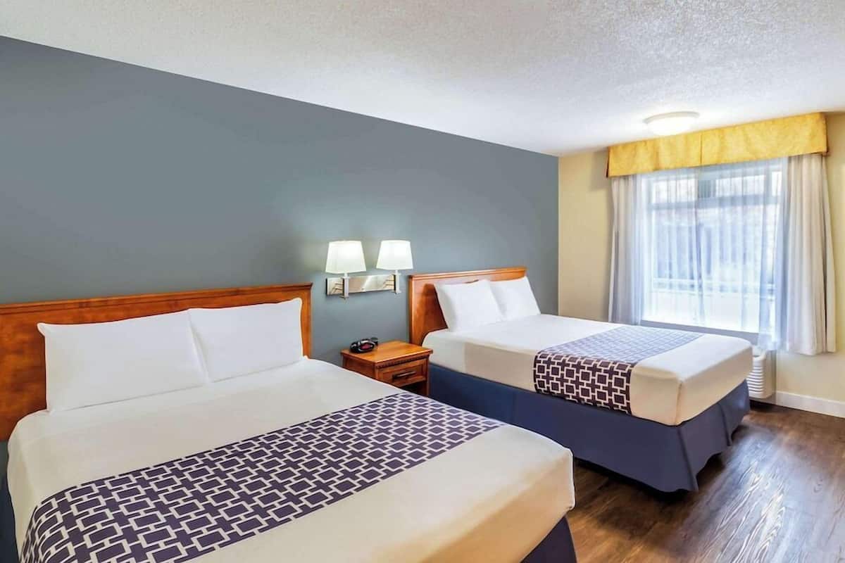 Une chambre d’hôtel avec deux lits, une table de chevet avec des lampes, une fenêtre avec des rideaux et une tête de lit en bois.