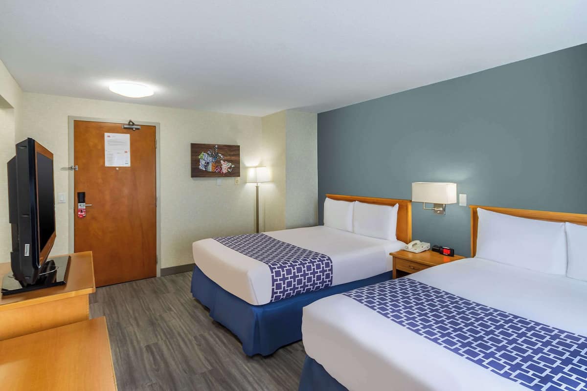 A hotel room with two beds, a desk, a television, and a door with a notice.